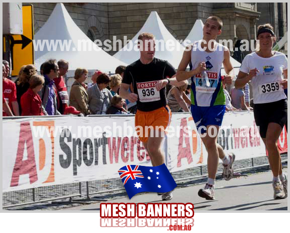 Three runners coming in to the last kilometres close to th temporary crowd control event barriers with banner signs attached.